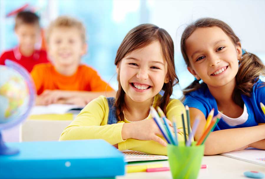 Two young girls smiling in a classroom.